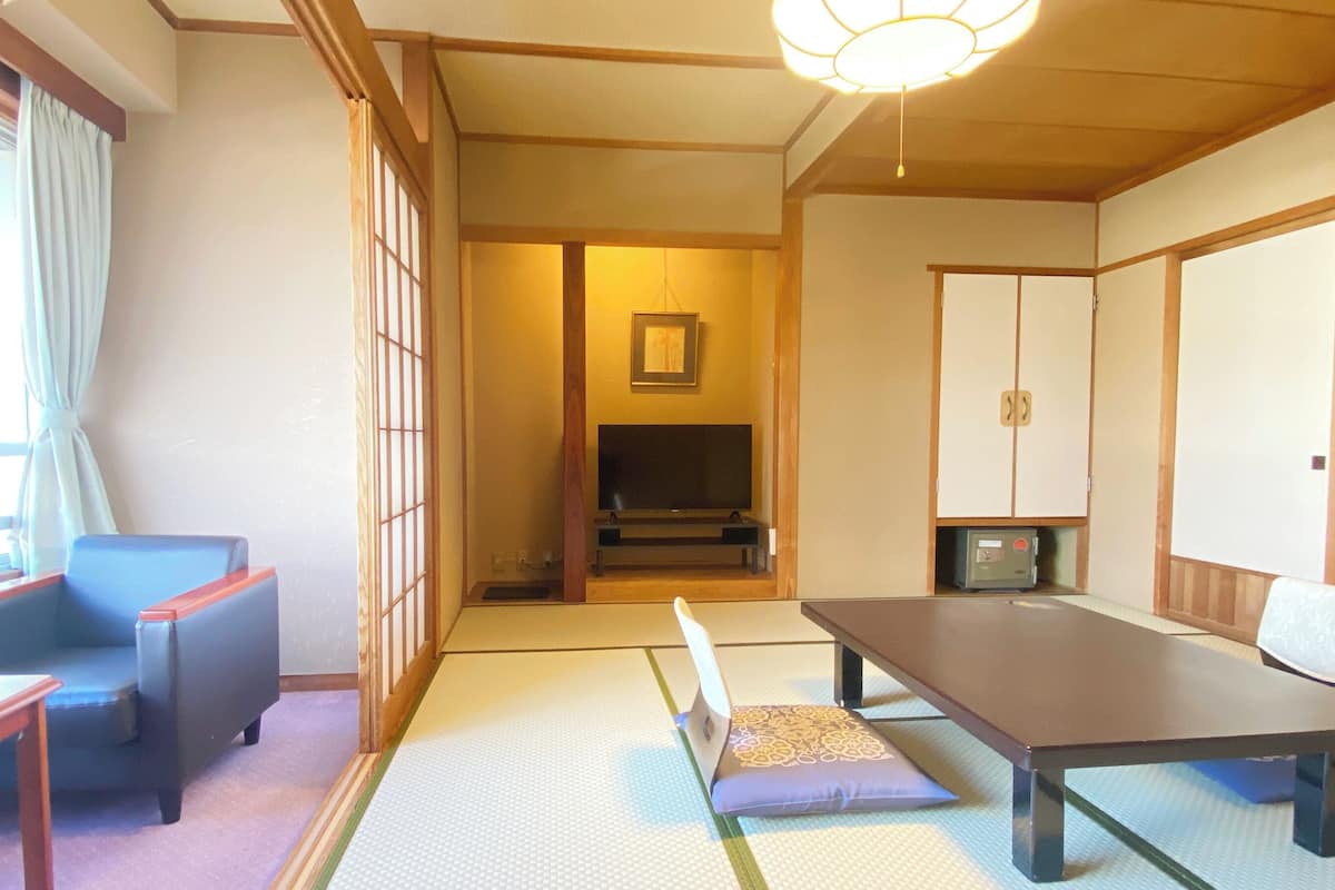 Ein traditioneller japanischer Raum mit Tatami-Bodenbelag, einem niedrigen Tisch, einer Couch und einem Fernseher.
