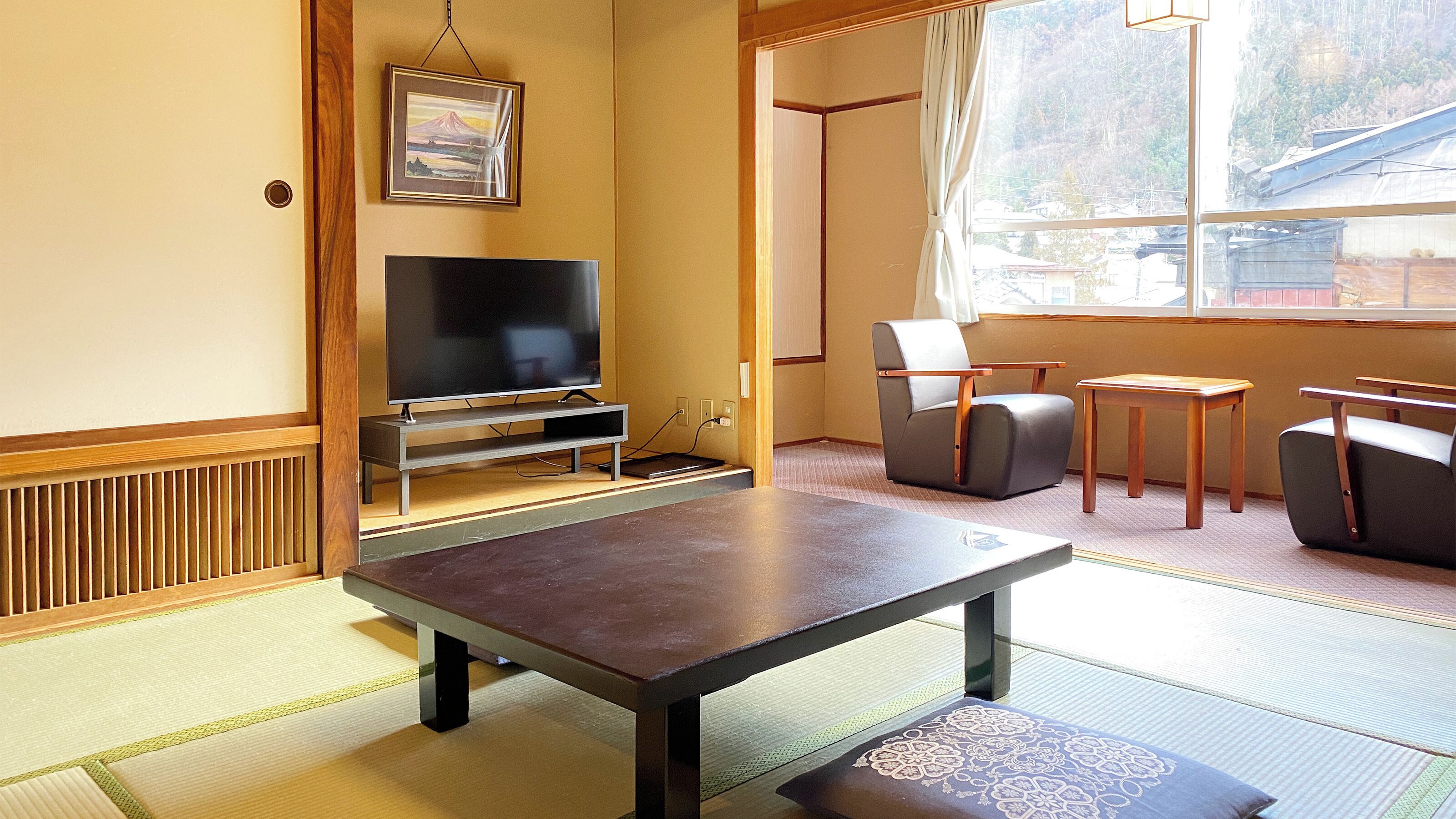 A room with tatami flooring, a television, a sofa, a chair, and a small table.