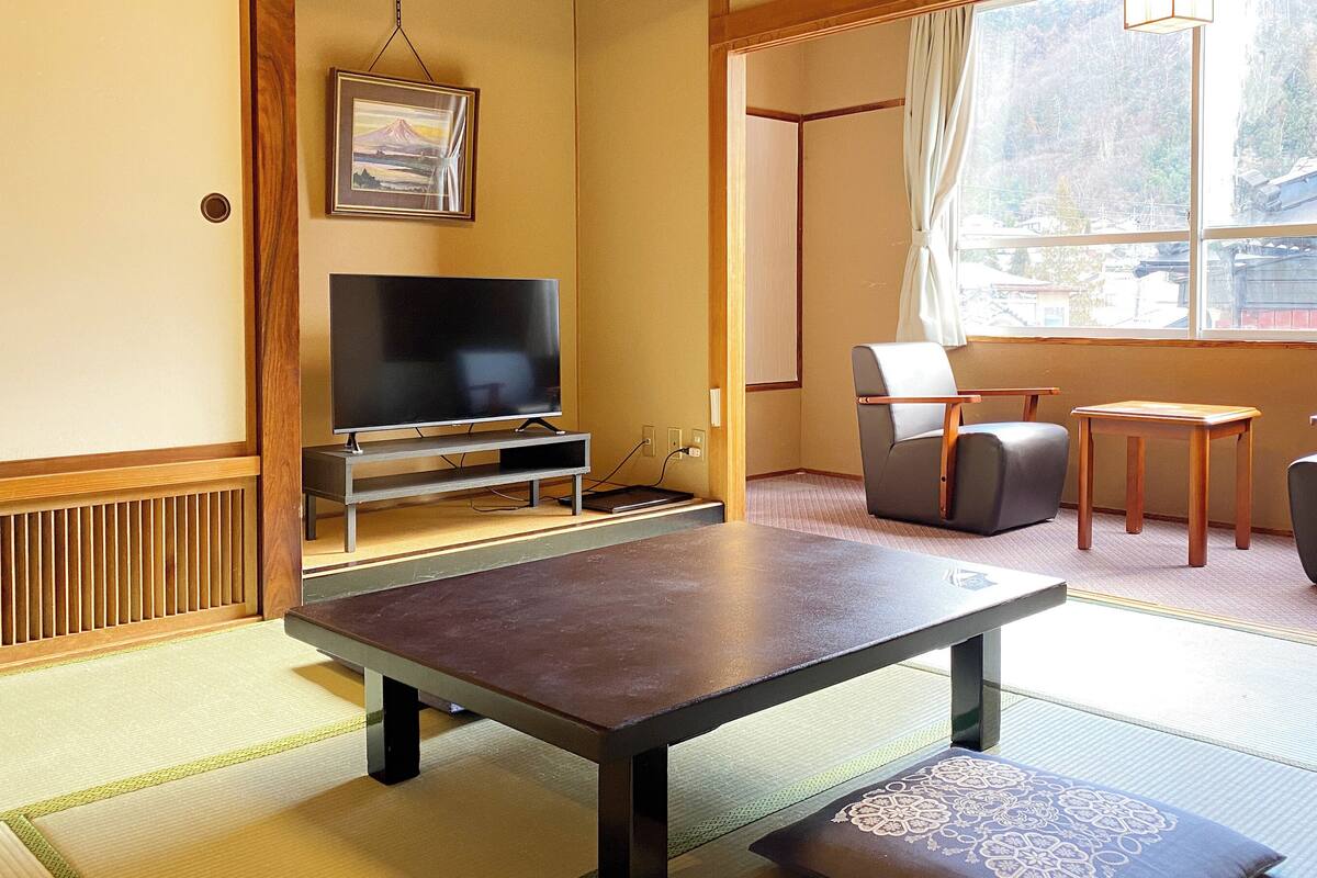 A room with tatami flooring, a television, a sofa, a chair, and a small table.