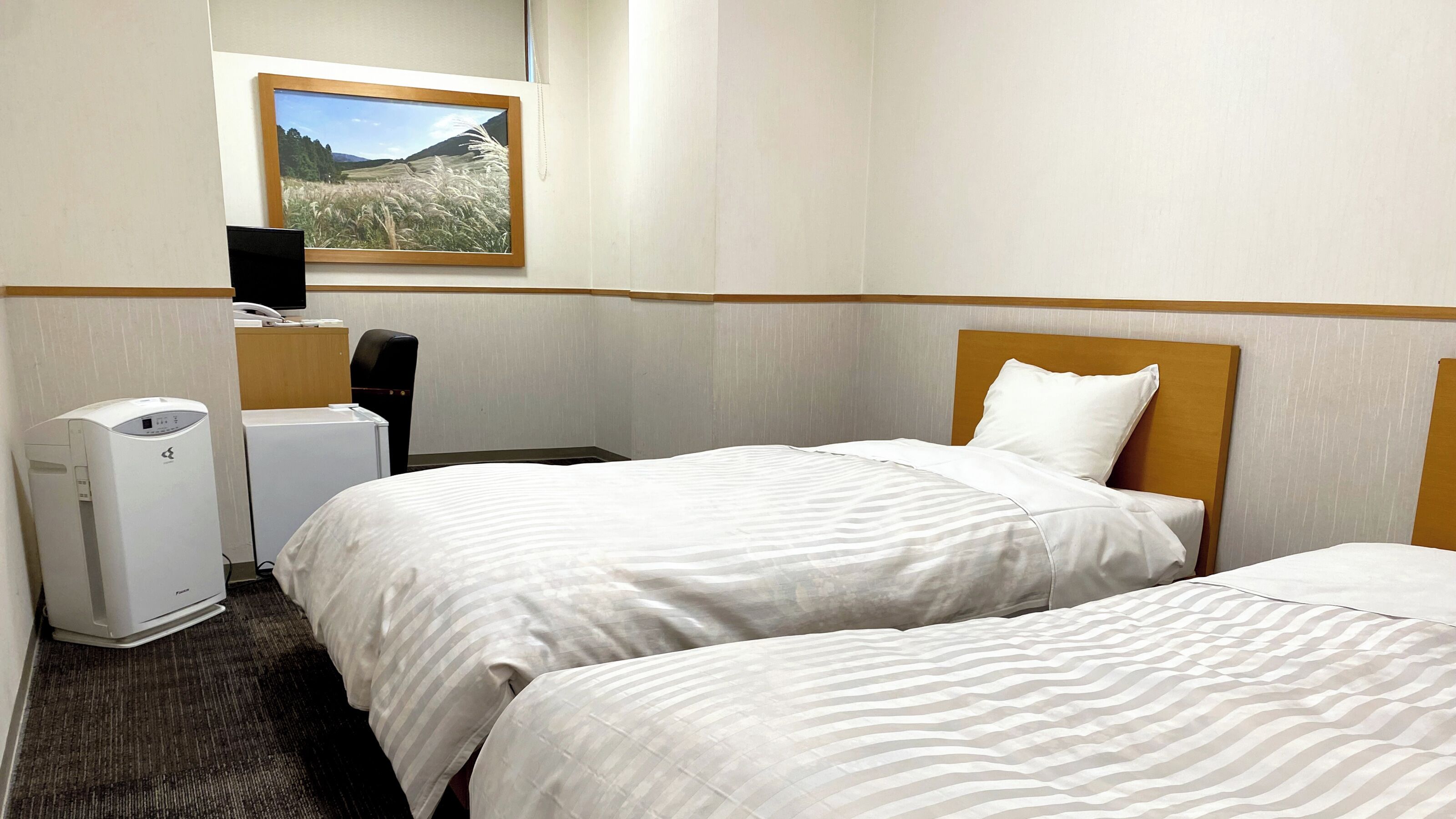 A hotel room with two beds, a desk, a chair, a heater, and a picture on the wall.