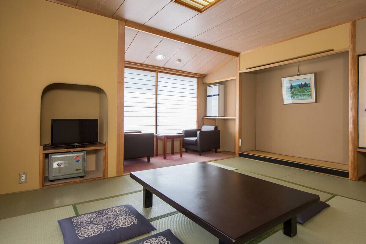 A traditional Japanese room with tatami flooring, a low table, a television, and a cabinet.