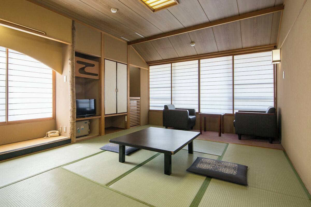 A traditional Japanese room with tatami flooring, a low table, seating, and sliding doors.