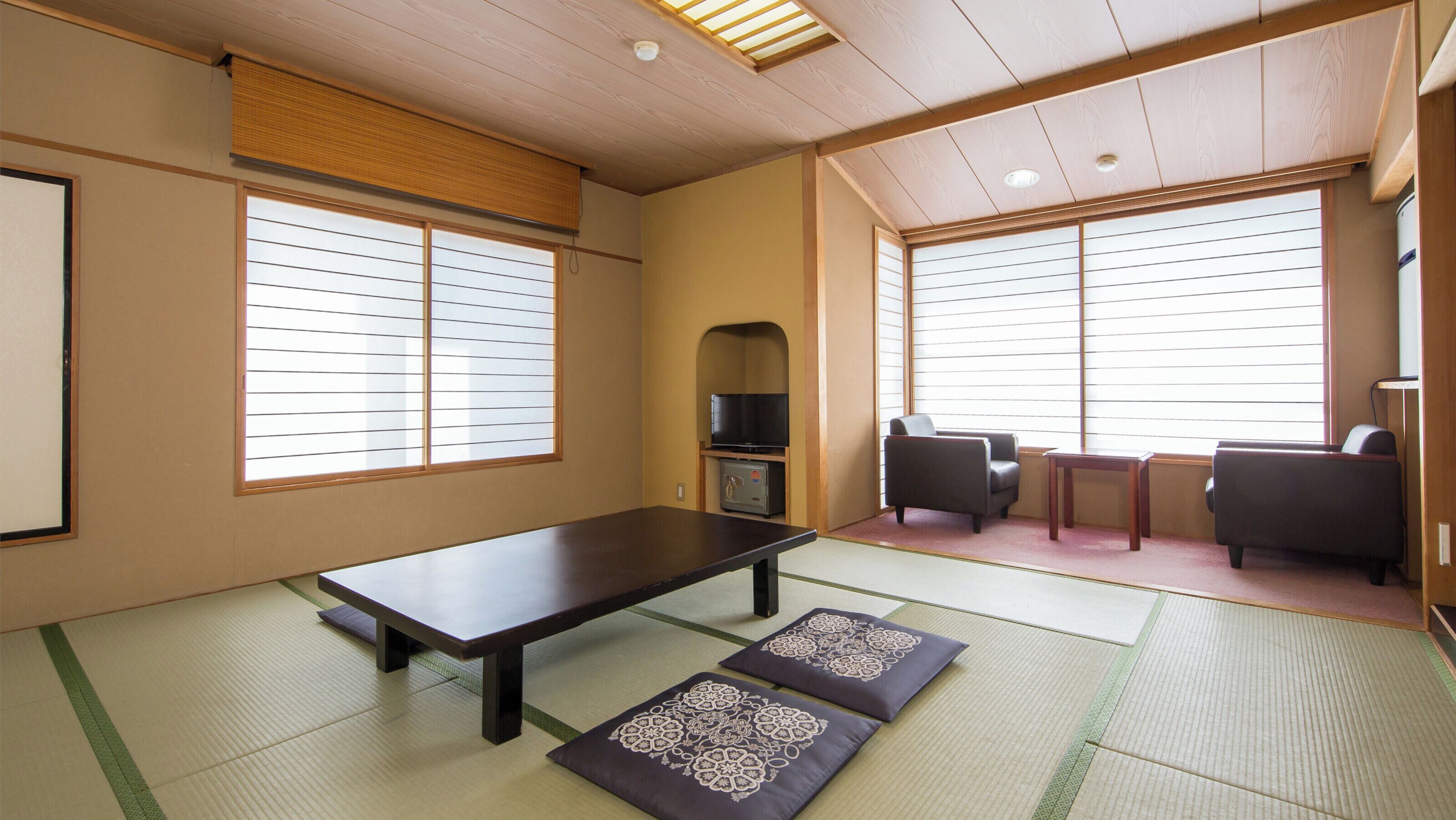 A tatami mat room with a low table, cushions, a television, and a sofa.