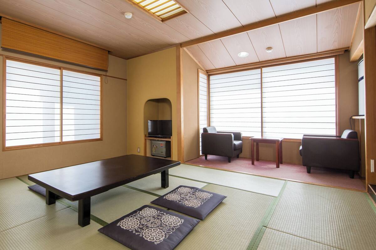 A tatami mat room with a low table, cushions, a television, and a sofa.