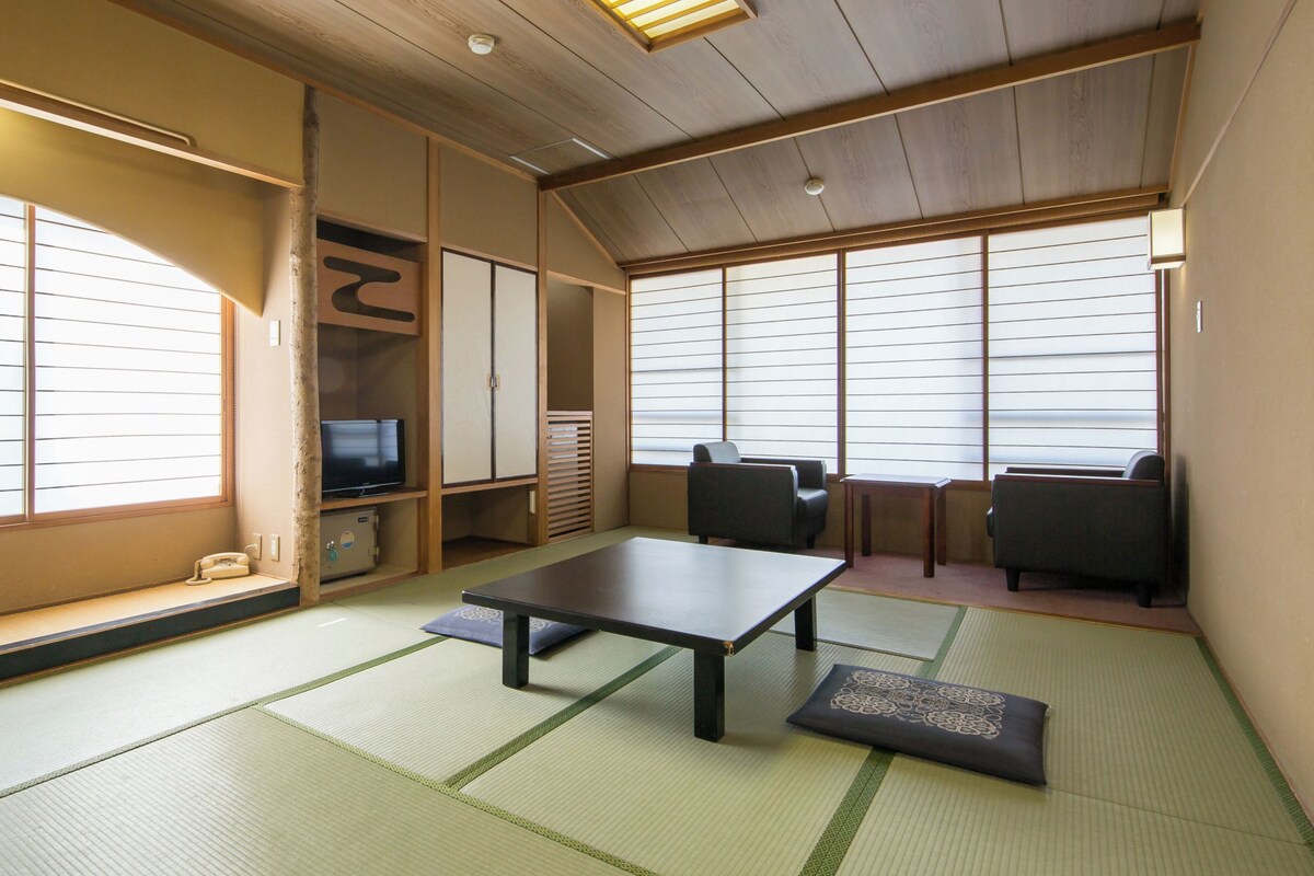 Una habitación japonesa tradicional con suelo de tatami, una mesa baja, asientos y puertas correderas.