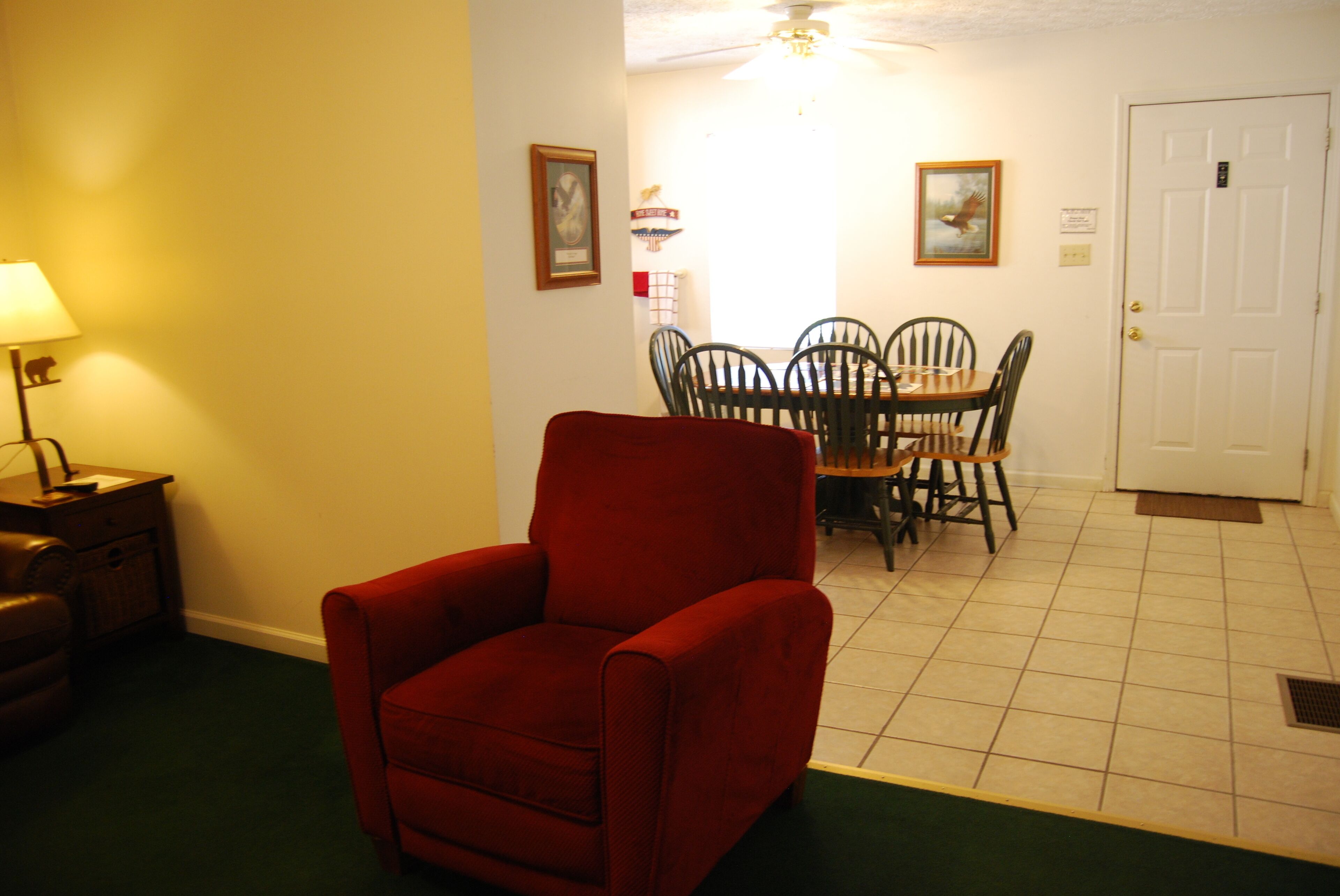 Una habitación con un sillón rojo, una mesa de comedor con sillas, una lámpara y una puerta.