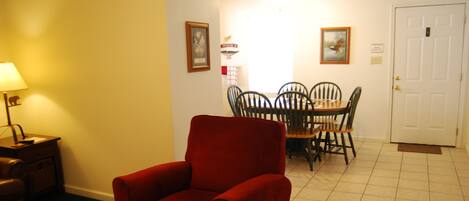 Una habitación con un sillón rojo, una mesa de comedor con sillas, una lámpara y una puerta.