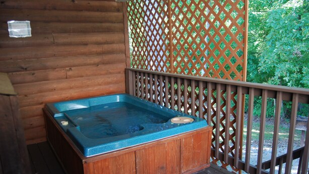 Un bain à remous en bois installé sur une terrasse, avec une clôture en treillis en arrière-plan.
