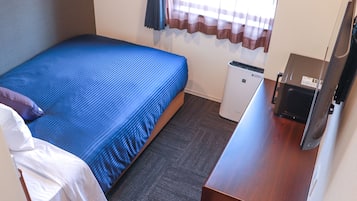 A small, neatly arranged hotel room with a single bed, a small desk, a television, and a compact trash bin.