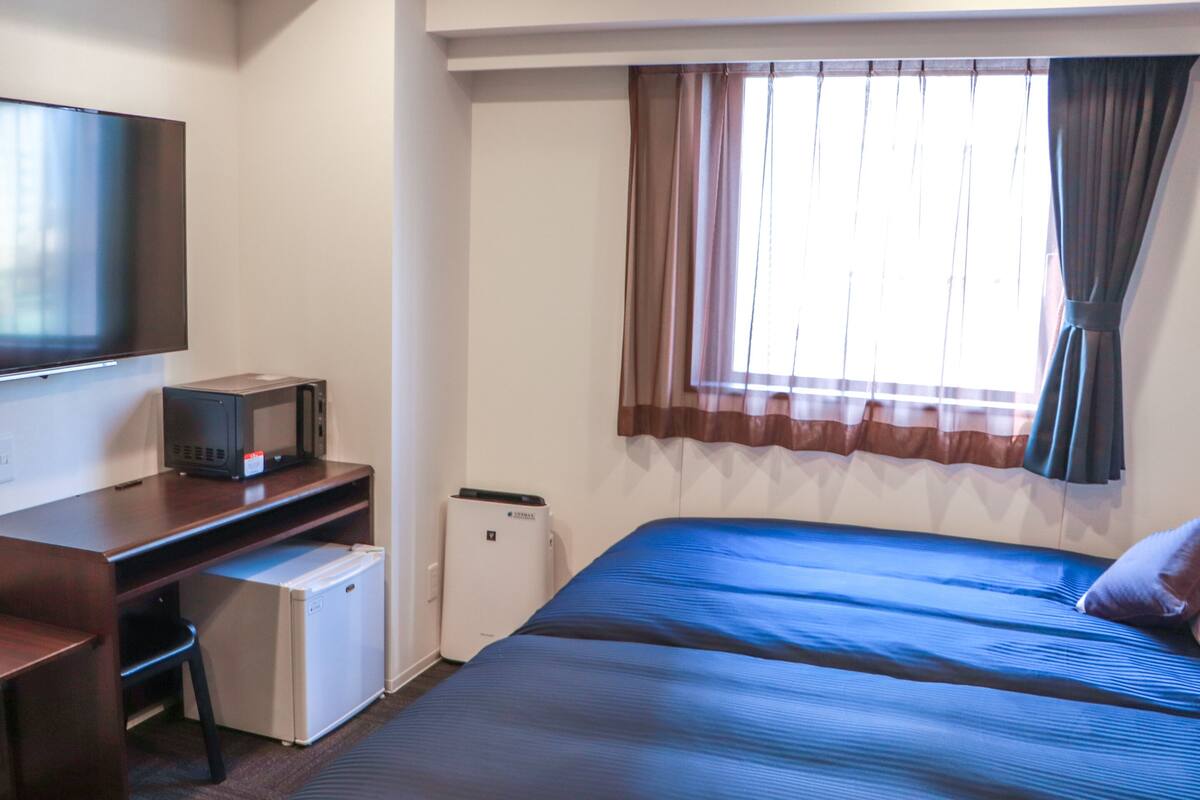 Ein Hotelzimmer mit Bett, Schreibtisch, Computer, Fernseher und Kühlschrank.