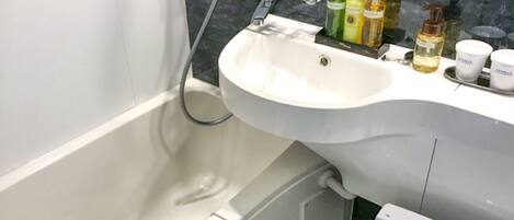 A bathroom with a white sink, a bathtub, and a toilet. There are toiletries on the sink counter.