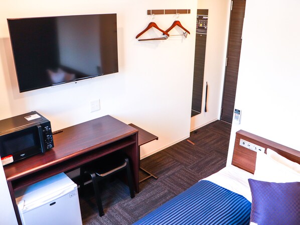 Una habitación de hotel con una cama, un escritorio con microondas, un televisor y un perchero.