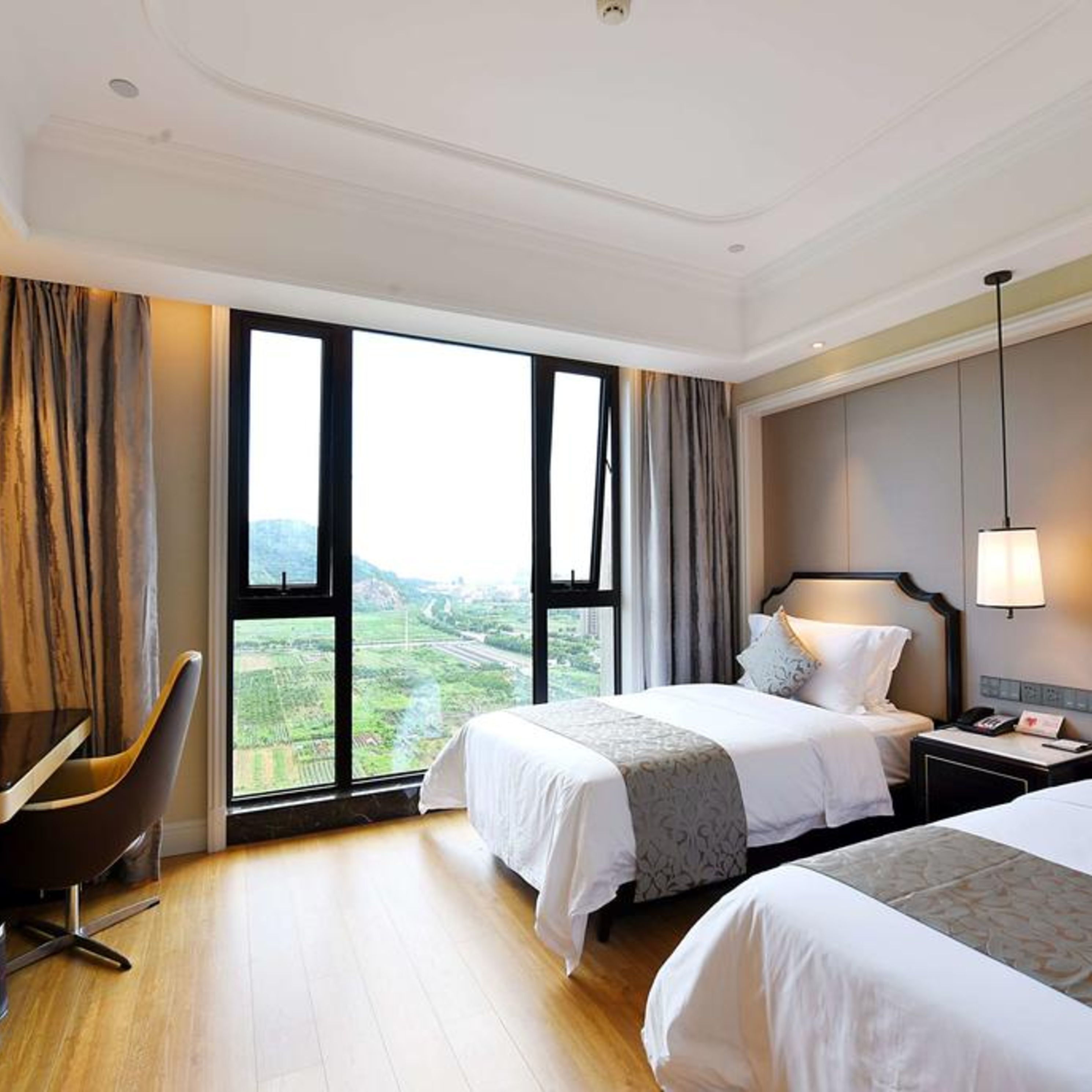 Een hotelkamer met twee bedden, een bureau en een groot raam met uitzicht op het landschap.