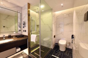 Ein modernes Badezimmer mit einer einachigen Duschkabine, einem großen Spiegel, einem мрамор-verkleideten Waschtisch und einer Toilette.