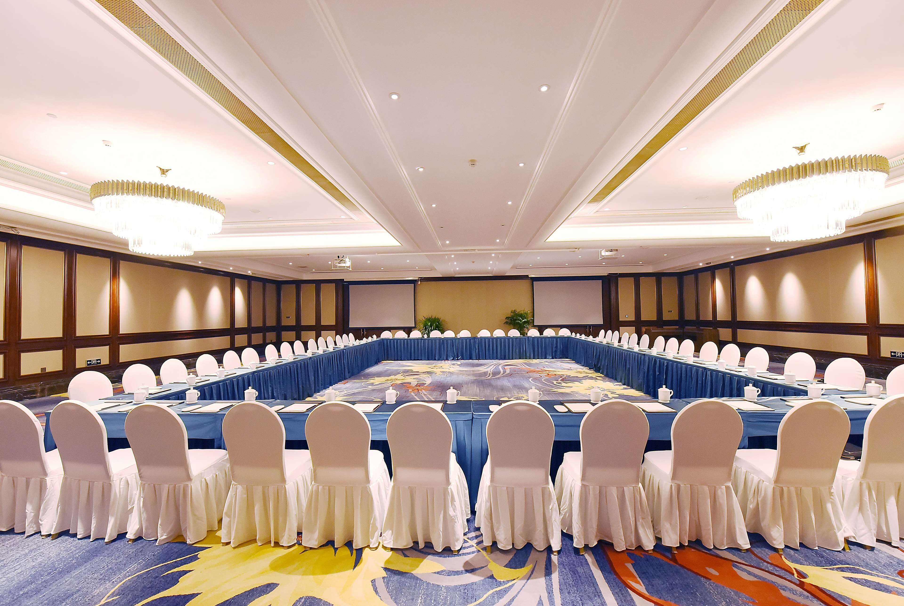 A large conference room with a long table, white chairs, and chandeliers.