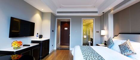 Une chambre d’hôtel dotée d’un grand lit, d’un téléviseur à écran plat, d’un bureau avec une machine à café et d’une salle de bain visible à travers une porte ouverte.