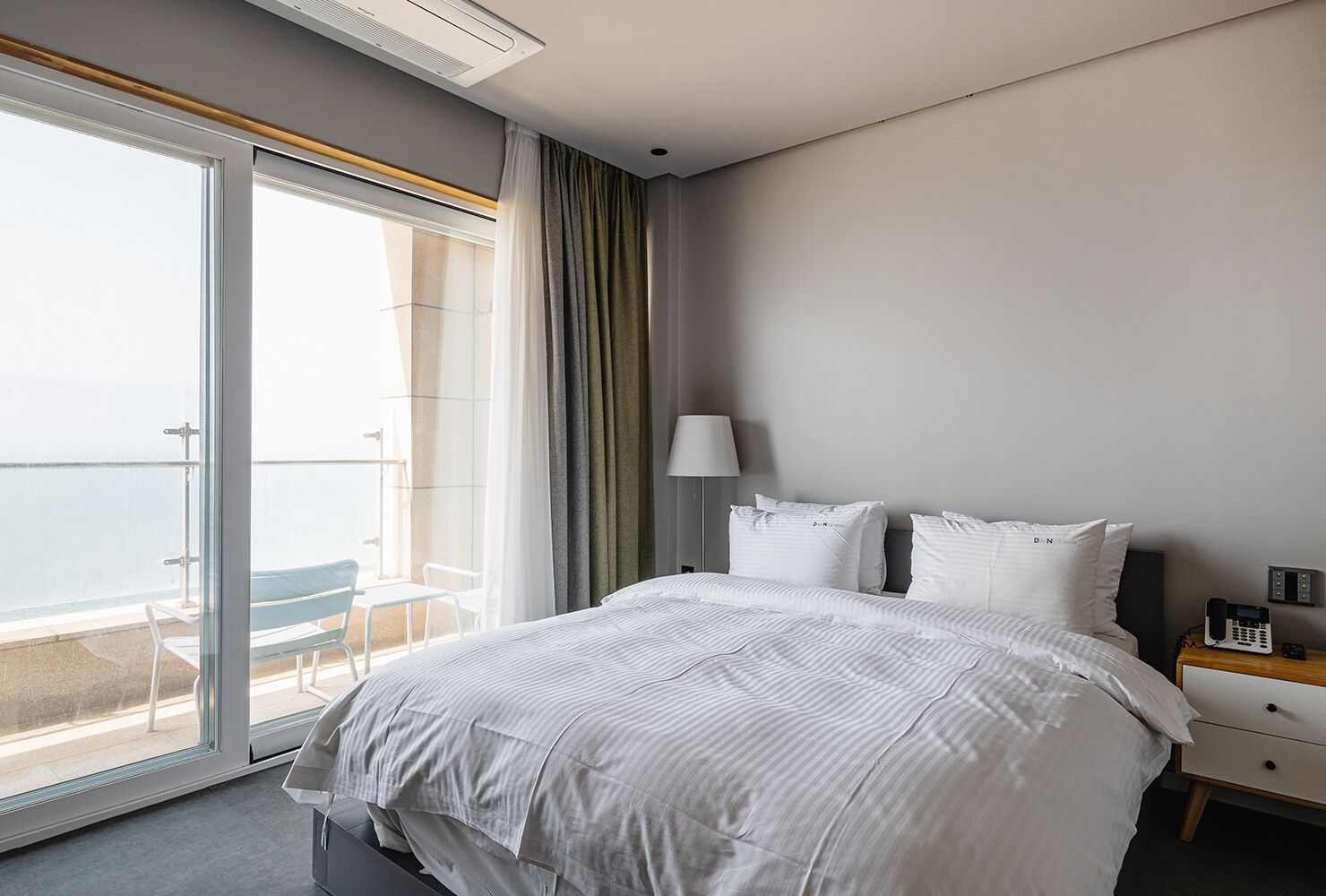 A hotel room with a large bed, a bedside table with a lamp, and a view of the balcony.
