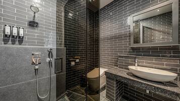 A modern bathroom with dark tiled walls, a glass shower enclosure, a white sink, and a large mirror.