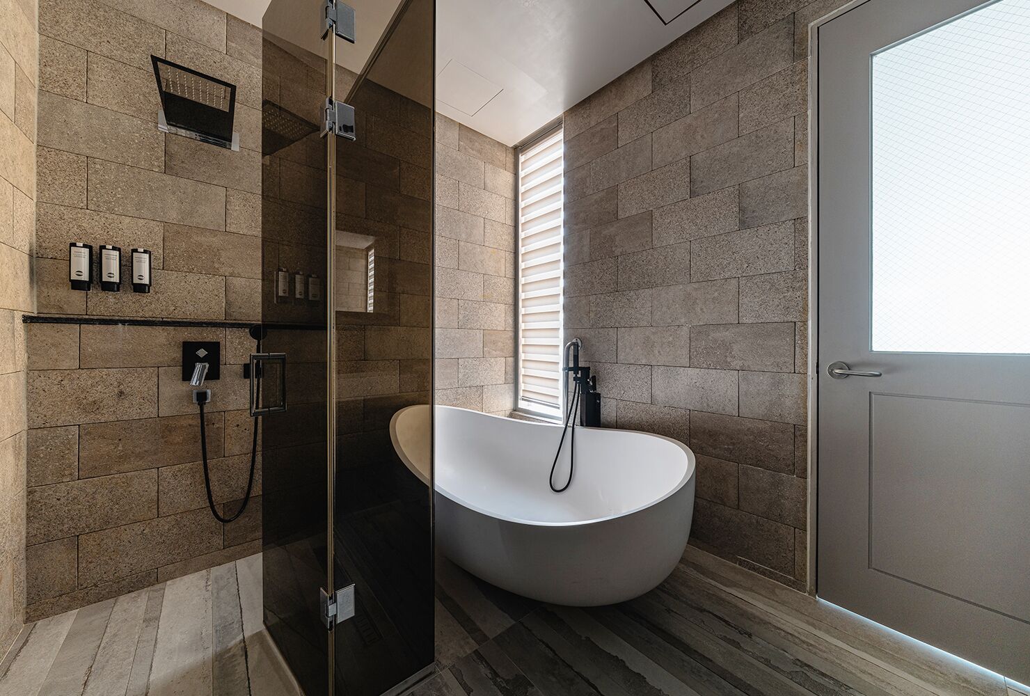 A modern bathroom with a freestanding bathtub, a glass-enclosed shower, and a door with a frosted glass panel.