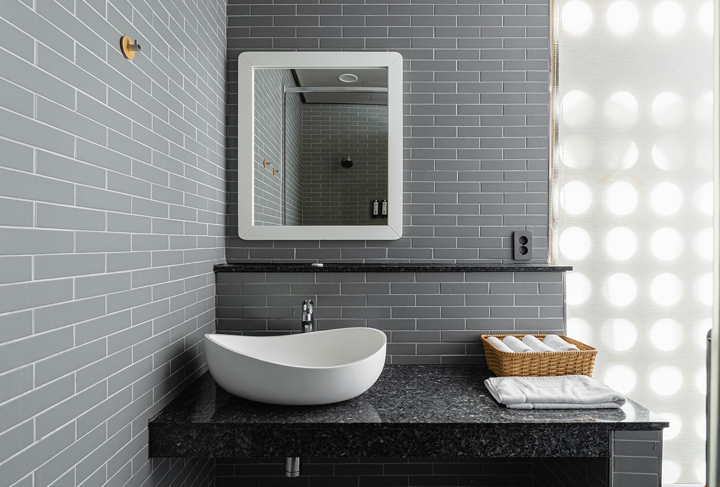 A modern bathroom with a white vessel sink, a black countertop, a mirror, and a wicker basket with towels.