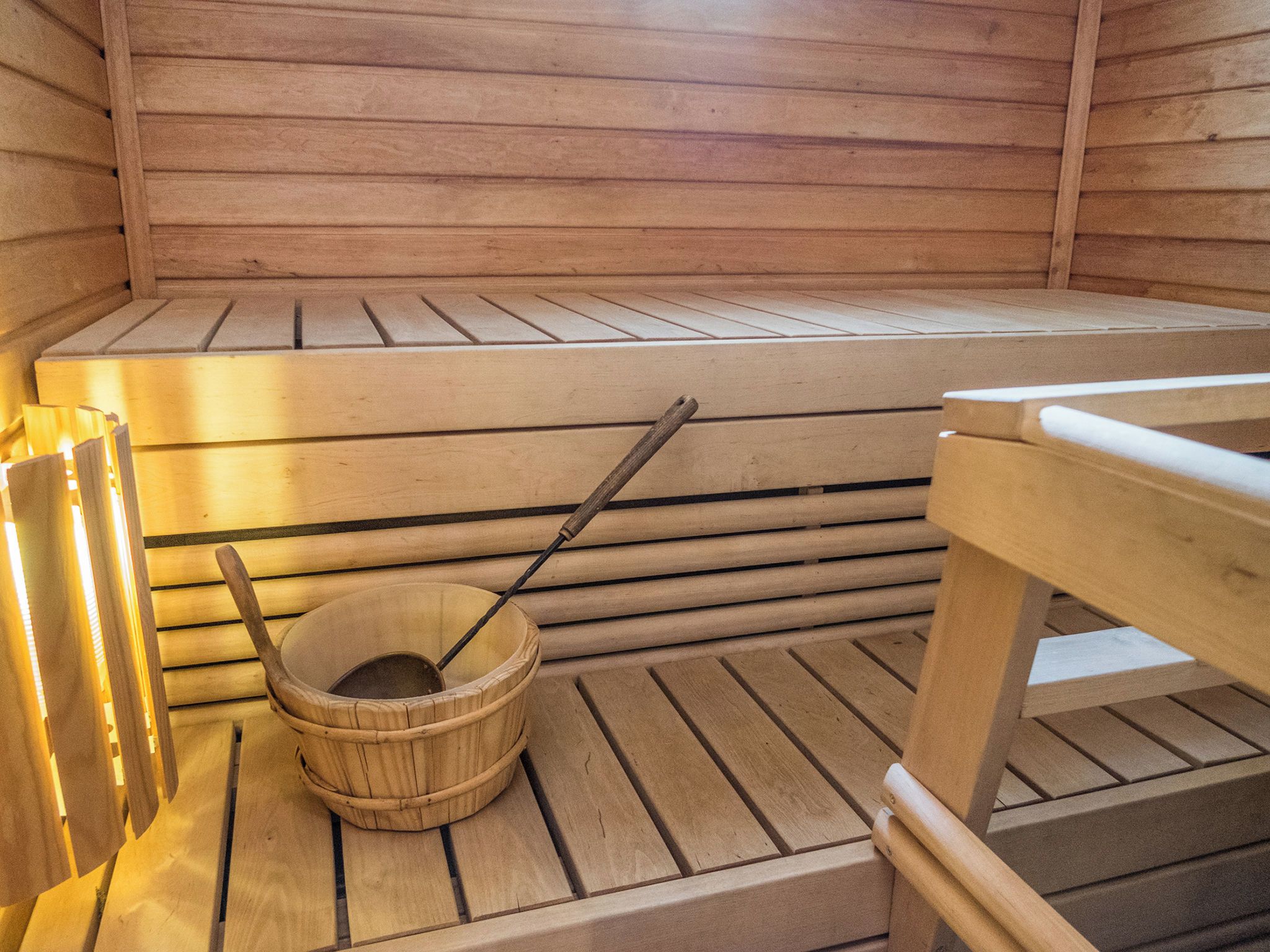 Una sauna con panche in legno e un catino di legno con una schiumarola.