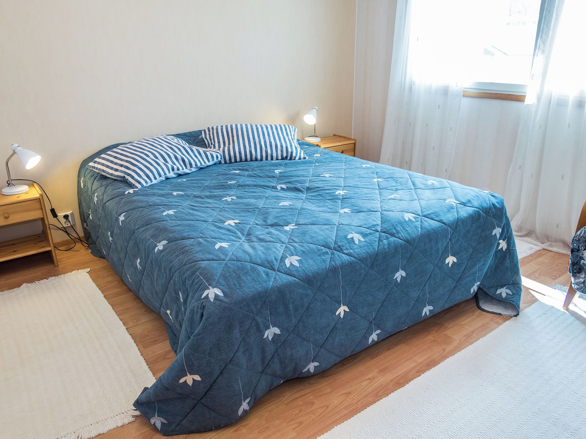 Quarto com cama, duas mesas de cabeceira, abajur e janela com cortinas.