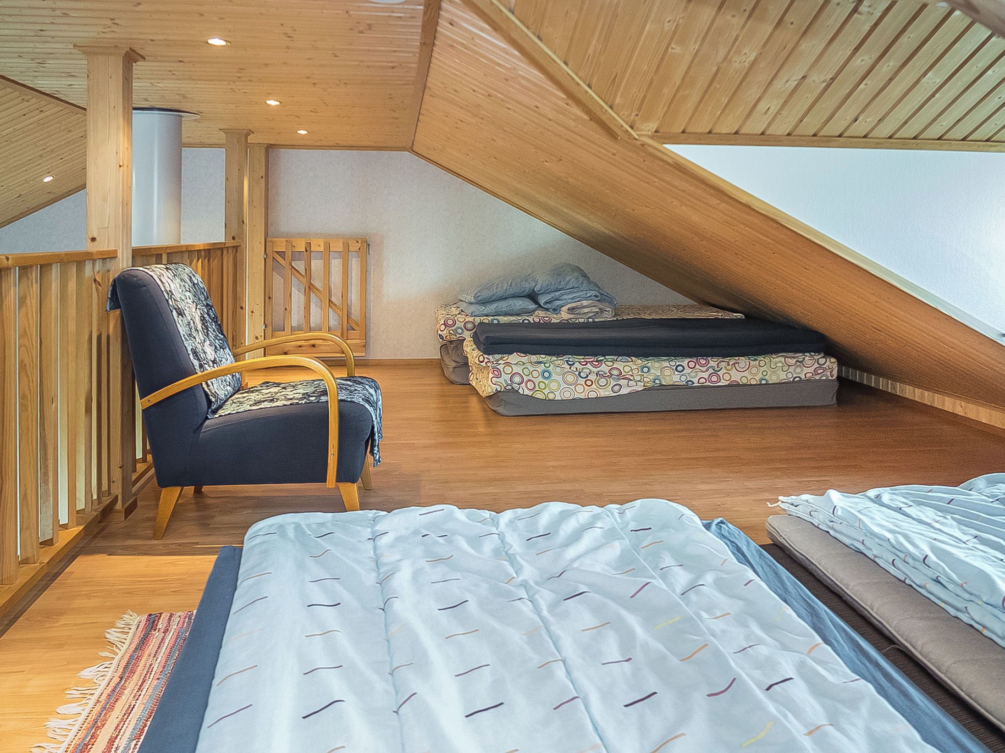 Une chambre mansardée avec un plafond en pente, des poutres en bois, un lit, une chaise et une petite table.