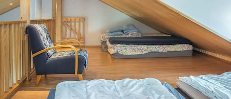 A loft bedroom with a sloped ceiling, wooden beams, a bed, a chair, and a small table.
