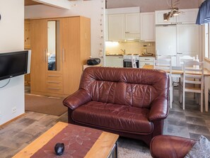 Una sala de estar con un sofá de cuero marrón, un televisor, una mesa de comedor con sillas y una zona de cocina al fondo.