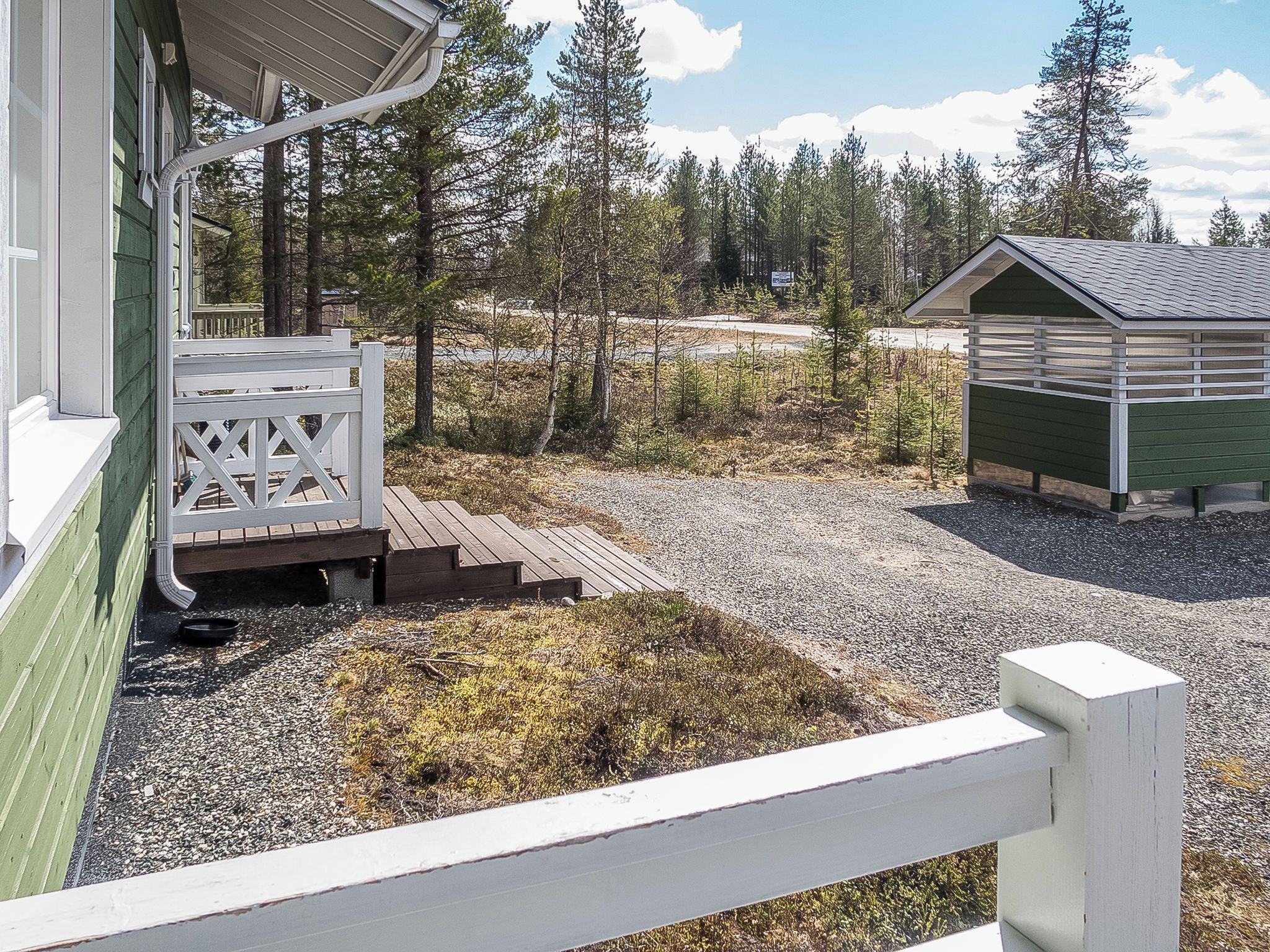 A wooden deck with a white railing, a gravel path, and a small shed in a forested area.