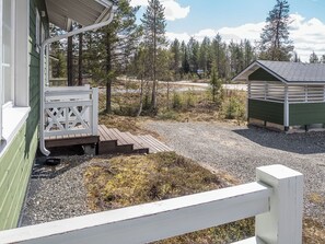 A wooden deck with a white railing, a gravel path, and a small shed in a forested area.