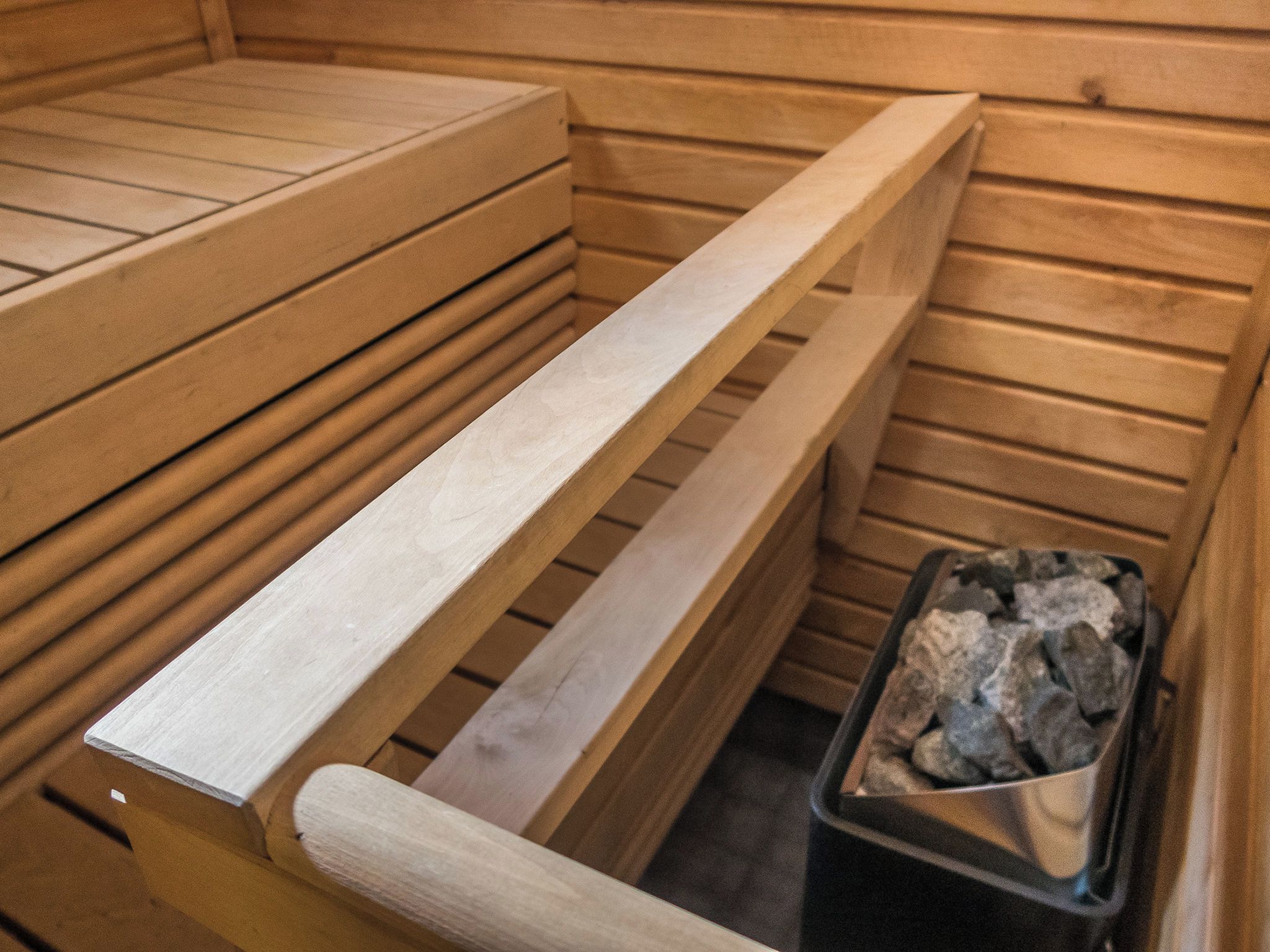 A sauna with wooden benches and a stone-filled container.
