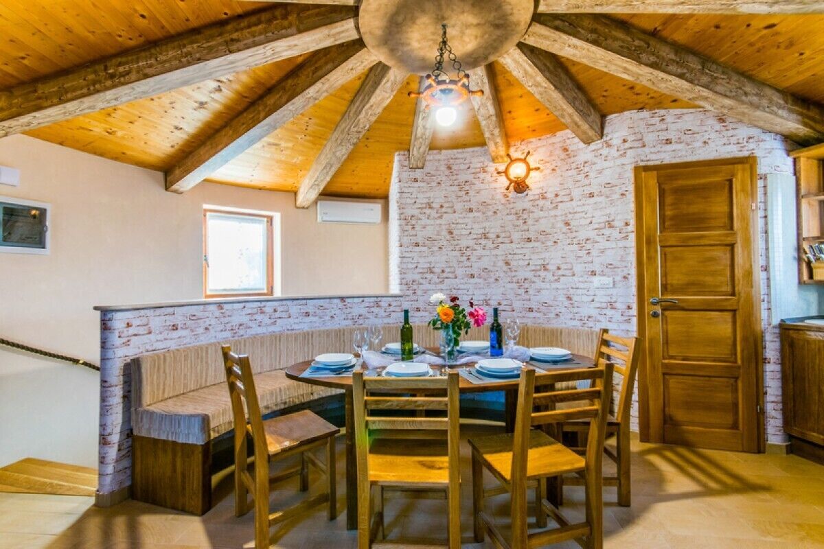 A dining area with a brick wall, wooden ceiling beams, and a round table set for six.
