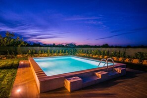 Ein rechteckiger Pool mit integriertem Whirlpool, umgeben von einer Holzterrasse und einer niedrigen Mauer.