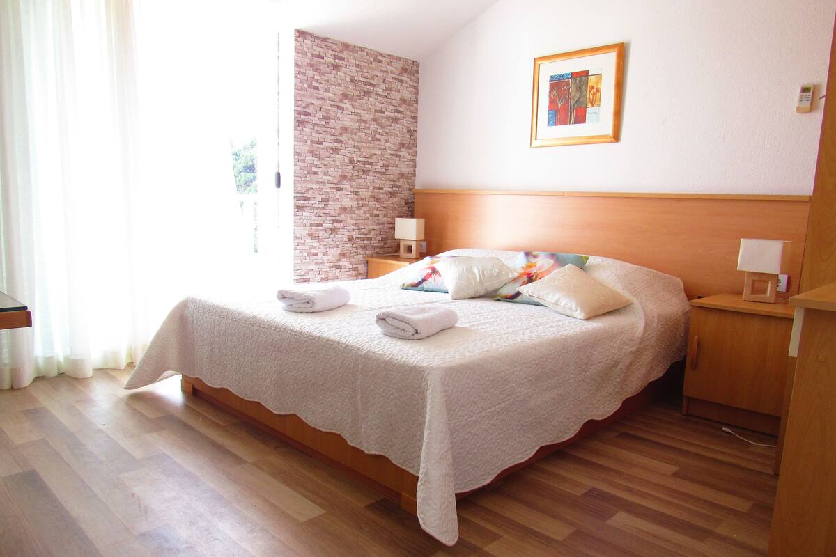 Un lit bien fait, avec du linge de lit blanc et des oreillers, une tête de lit en bois, un mur décoratif en briques, un tableau encadré et une table de chevet avec une lampe.