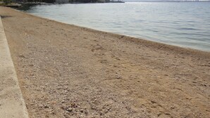 A beach with pebbles, a clear sky, and distant mountains. - Apartmani Roko (Kastela)