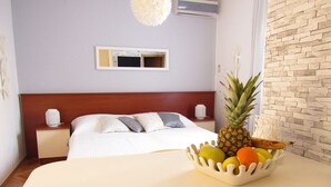 A hotel room with a bed, a nightstand, a fruit bowl on a table, and a brick wall. - Apartmani Roko (Kastela)
