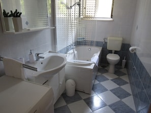 Une salle de bain équipée d’un lavabo, d’une baignoire, de toilettes et d’une fenêtre avec des stores.