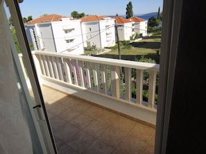 Un balcon doté d’une balustrade blanche, d’un sol carrelé et offrant une vue sur des bâtiments blancs aux toits rouges, qui se dressent à l’arrière-plan.