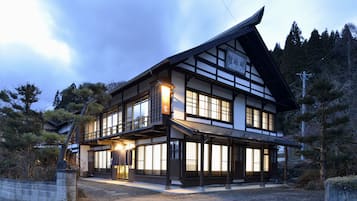 A traditional Japanese building with a sloped roof and multiple windows, surrounded by trees and a stone wall.