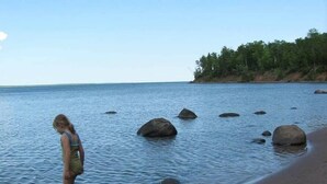 A beach with calm water, large rocks, and a person standing in the water. - Driftwood Cottage: Your Gateway to Lake Superior & Apostle Islands (Washburn)
