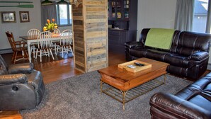 A living room with a leather sofa, a dining table with chairs, and a kitchen area with cabinets. - Driftwood Cottage: Your Gateway to Lake Superior & Apostle Islands (Washburn)