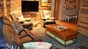 A cozy living room with leather sofas, a wooden coffee table, and a flat-screen TV mounted on the wall. - Driftwood Cottage: Your Gateway to Lake Superior & Apostle Islands (Washburn)