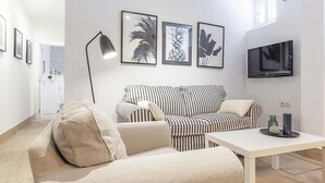 A modern living room with a sofa, a coffee table, and a TV mounted on the wall. There are framed pictures on the wall and a floor lamp. - ELEGANT DESIGN APARTMENT! 2 BED -SEVILLA- WIFI - 5 PAX (Sevilla)