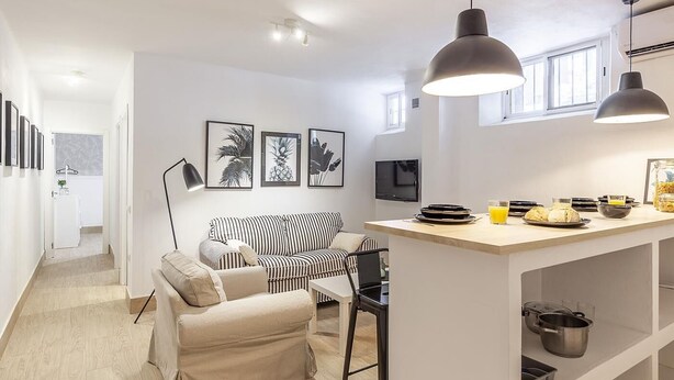 A modern kitchen with a central island, a dining area with a striped sofa, and a hallway leading to a bathroom. - ELEGANT DESIGN APARTMENT! 2 BED -SEVILLA- WIFI - 5 PAX (Sevilla)