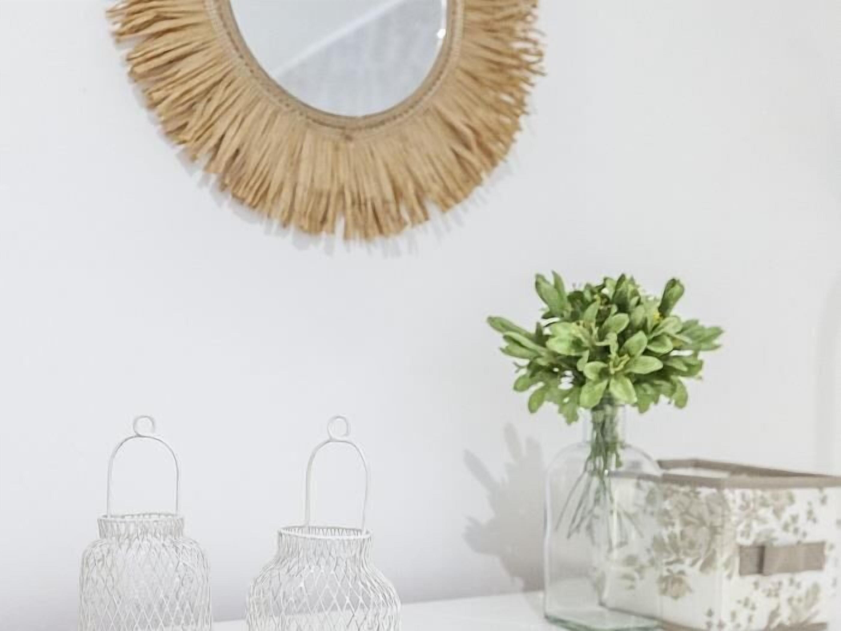 A white wall with a round mirror and two wireframe lanterns.
