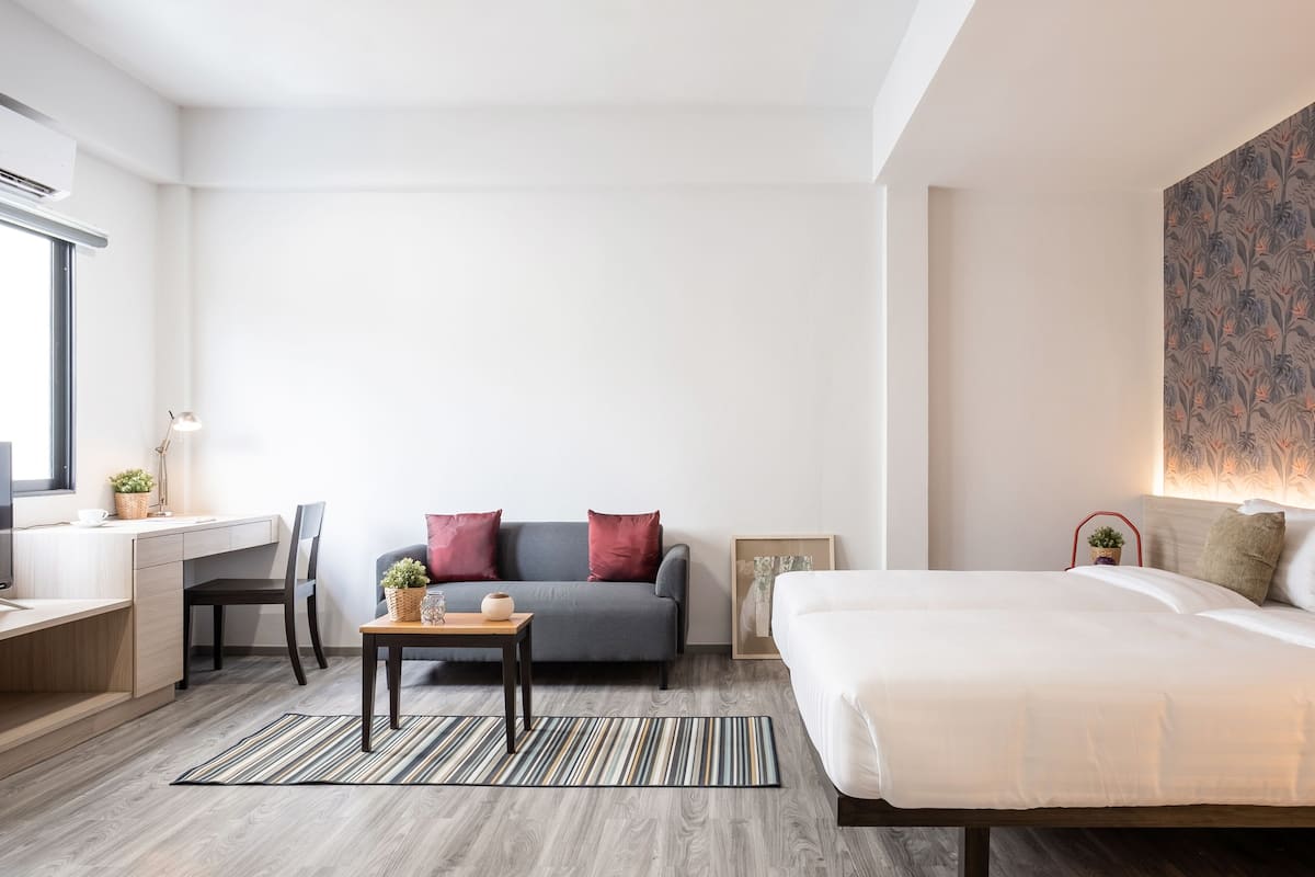 A modern hotel room with a bed, a desk, a sofa, and a chair.