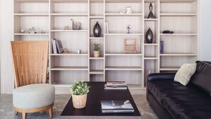Una sala moderna con una mesa de centro de madera oscura, un sofá de cuero negro y una silla de madera. Se observa una estantería llena de objetos decorativos y libros.