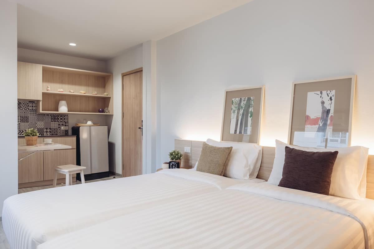 A modern hotel room with a large bed, a small kitchenette, and two framed artworks on the wall.