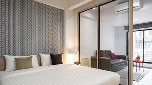 Habitación de hotel con una cama grande, papel tapiz estampado, puerta corrediza de vidrio a un balcón y una pequeña mesa con una planta.